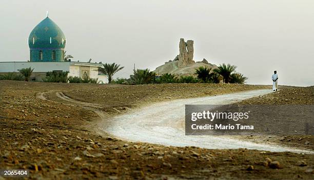 Man walks down a road in the shadow of a Mesopotamian ziggurat and a shrine to the prophet Abraham June 8, 2003 in Borsippa, Iraq. The ziggurat, a...