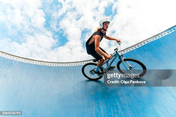 daring mid adult male cyclist riding the edge of a skate park bowl under a bright cloud-filled sky - hochgefühl stock-fotos und bilder