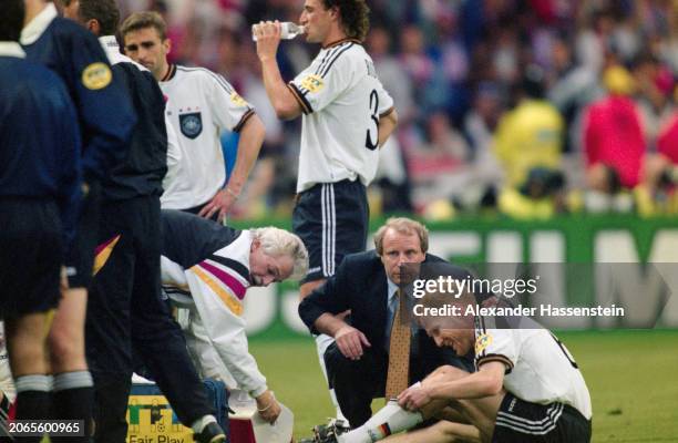 German football manager Berti Vogts crouches beside German footballer Matthias Sammer as Slovenian-born German footballer Fredi Bobic drinks from a...