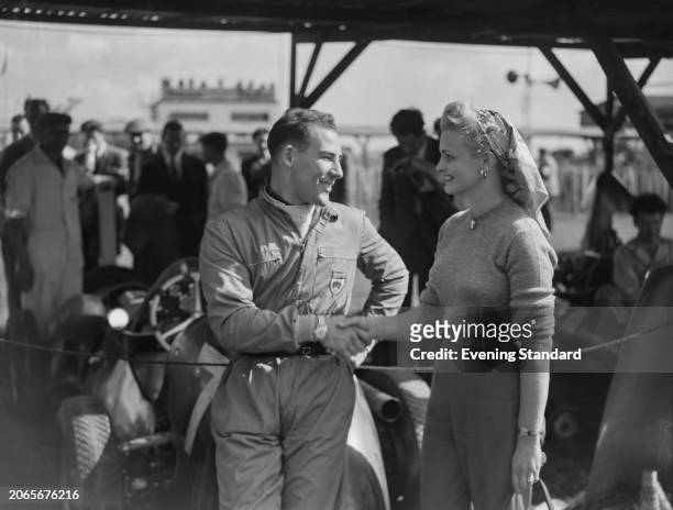 British racing driver Stirling Moss shaking hands with a woman named as Mrs Cooper at Goodwood Circuit where he is competing in the Madgwick and...