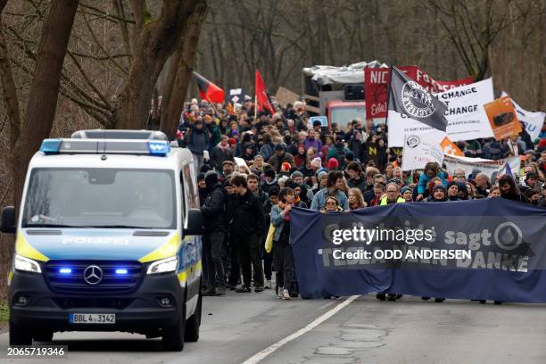 Police car drives ahead as demonstrators march with a banner reading 'Gruenheide says 'No thank you' during a protest against the expansion plan for...