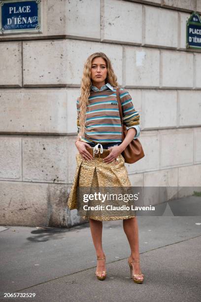 Emili Sindlev wears brown and blue striped t-shirt, gold skirt, brown belt, brown bag, gold sandals, outside Miu Miu, during the Womenswear...