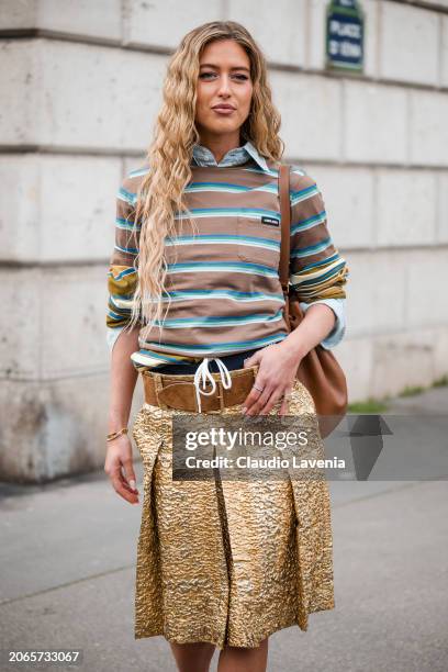 Emili Sindlev wears brown and blue striped t-shirt, gold skirt, brown belt, brown bag, outside Miu Miu, during the Womenswear Fall/Winter 2024/2025...