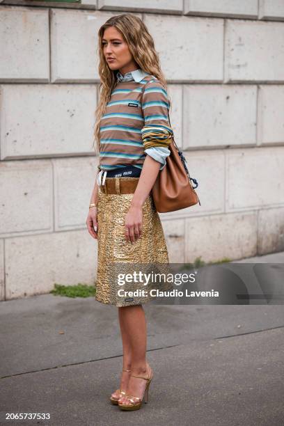 Emili Sindlev wears brown and blue striped t-shirt, gold skirt, brown belt, brown bag, gold sandals, outside Miu Miu, during the Womenswear...