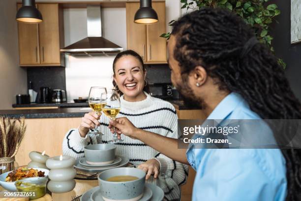 multi-ethnic couple at home having a date night. real couple enjoying dinner and drinking white wine - young couple date night wine stock pictures, royalty-free photos & images