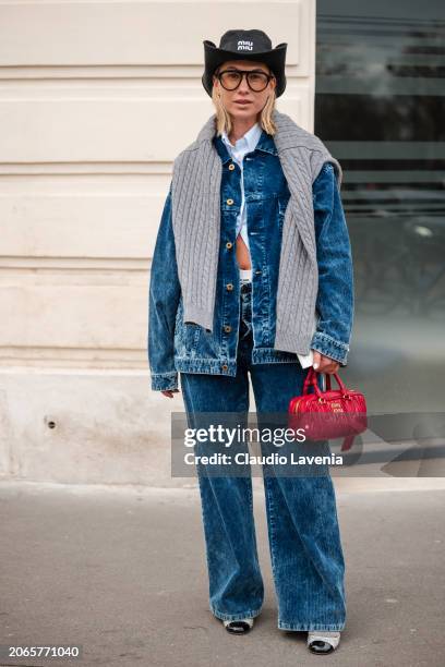 Karin Teigl wears light blue striped shirt, blue denim jacket, blue jeans, black Miu Miu hat, grey jumper, red Miu Miu bag, outside Miu Miu, during...