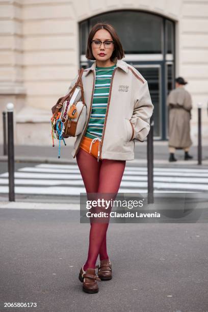 Guest wears green striped top, beige Miu Miu jacket, beige Miu Miu bag, orange underwear, red tights, brown loafers, outside Miu Miu, during the...