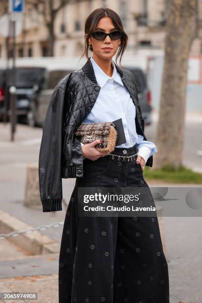 Guest wears light blue shirt, black decorated baggy jeans, black leather quilted jacket, brown checked Chanel bag, outside Chanel, during the...