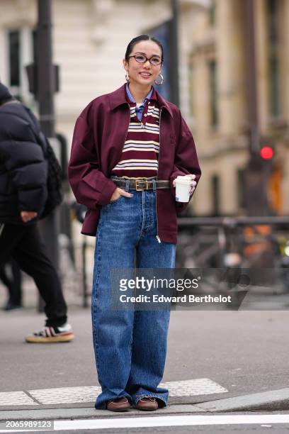 Yoyo Cao wears golden earrings, a burgundy oversized jacket , a striped polo shirt, a belt, blue denim pants / jeans , brown leather loafers shoes,...