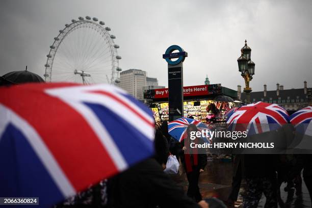 Tourists shelter from the rain as they walk over Westminster Bridge, with the Houses of Parliament in the background, in London on March 10, 2024.