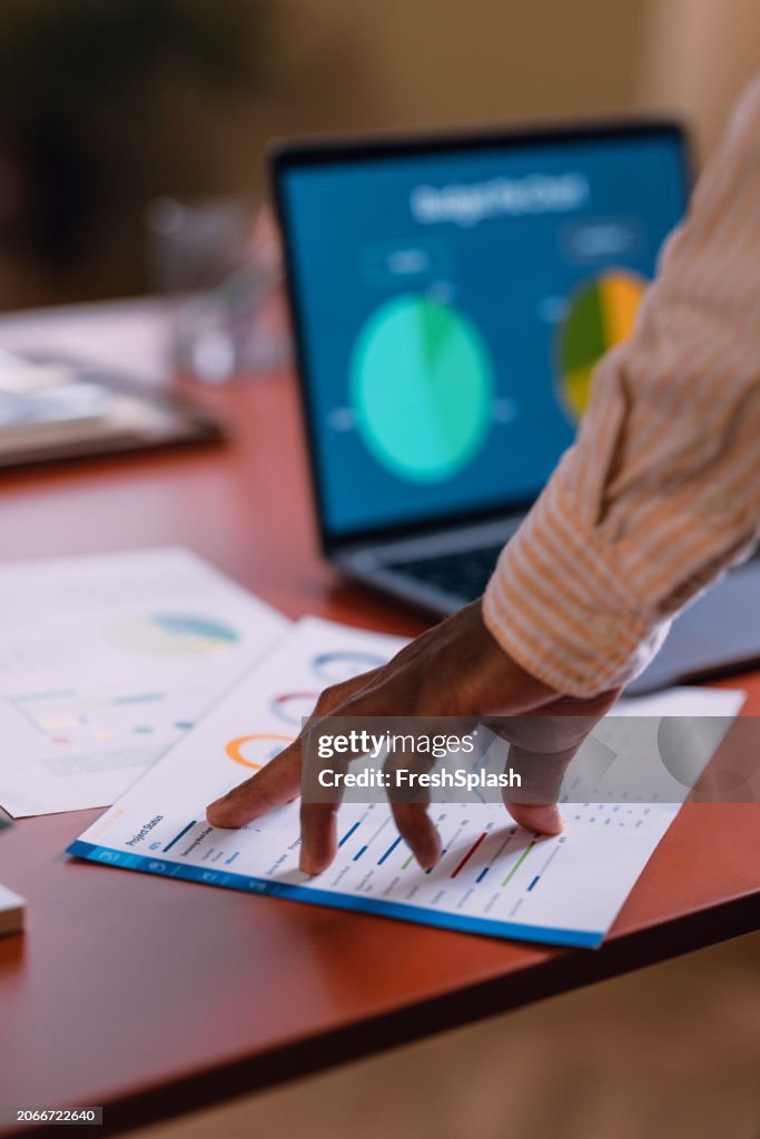 Business Professional Analyzing Data Charts on Paper Next to Laptop