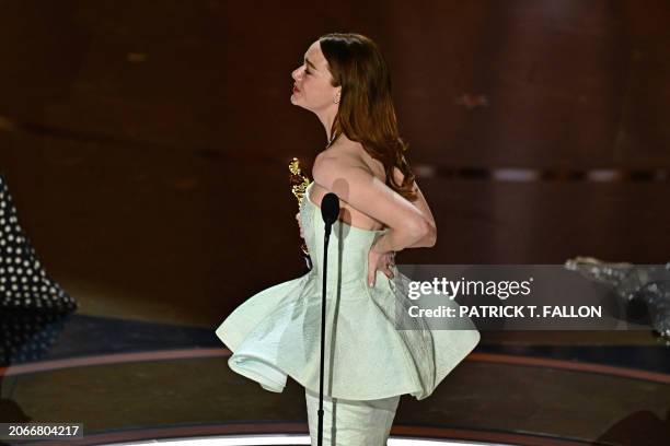Actress Emma Stone holds the back of her dress as she accepts the award for Best Actress in a Leading Role for "Poor Things" onstage during the 96th...