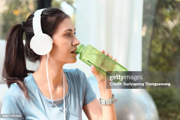 beautiful young woman drinking water while doing exercise or yoga in living room at home. healthy lifestyle or sports training concept. - flatten the curve imagens e fotografias de stock