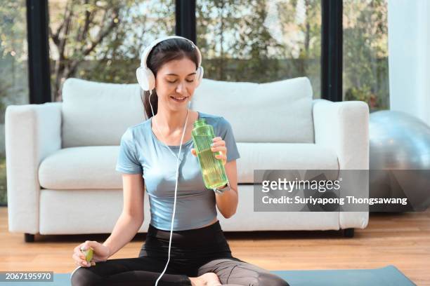 beautiful young woman drinking water while doing exercise or yoga in living room at home. healthy lifestyle or sports training concept. - kurve abflachen stock-fotos und bilder