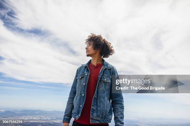low angle view of young man wearing denim jacket standing against sky - jeansjacke stock-fotos und bilder