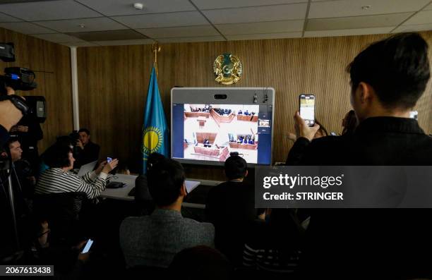Members of the media gather in front of a screen showing a live courtroom broadcast during the preliminary hearing in the trial of Kazakh former...