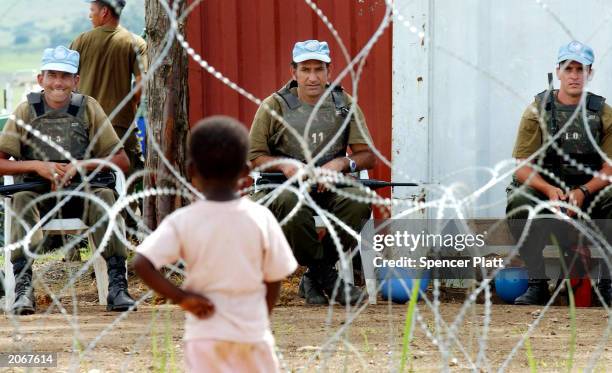 Young boy looks through concertina wire at three Uruguayan United Nations peacekeepers at a refugee camp June 9, 2003 in Bunia, Democratic Republic...