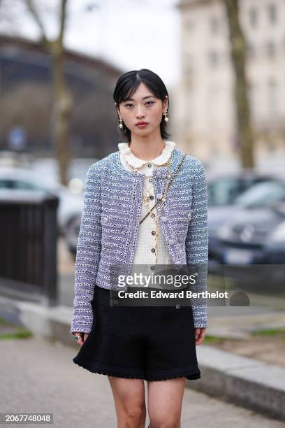 Guest wears earrings, a white pullover with ruffled collar, a pastel pale striped tweed jacket , a black mini skirt , outside Chanel, during the...