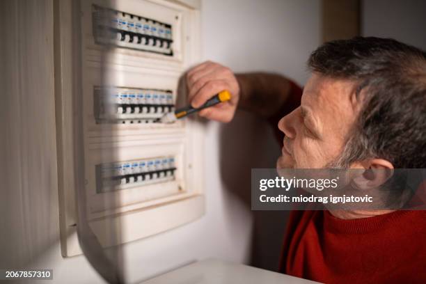 mann überprüft den sicherungskasten in seiner wohnung - schaltschrank stock-fotos und bilder
