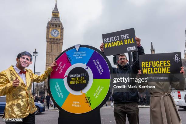 An actor wearing a Rishi Sunak mask and dressed as a gameshow host spins a 'wheel of misfortune' in Parliament Square during an event staged by...