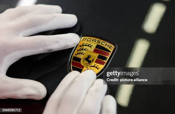 March 2024, Saxony, Leipzig: An employee attaches the brand logo to a Porsche at the Leipzig plant. Sports and off-road vehicle manufacturer Porsche...