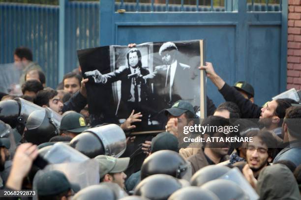 Iranian hardline protesters hold a picture of a scene from the movie "Pulp Fiction" showing actors pointing their guns, as riot policemen stand guard...