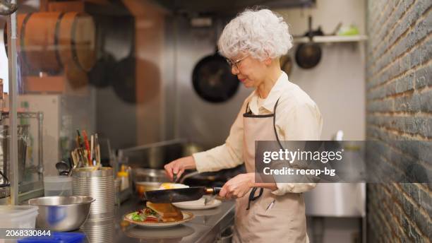 femme âgée travaillant dans la cuisine commerciale d’un café restaurant - retraités qui travaillent photos et images de collection