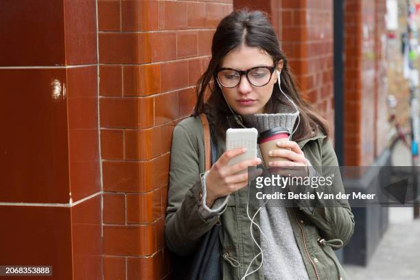 woman is listening to phone, with earplugs, in urban street. - recreational equipment stock pictures, royalty-free photos & images