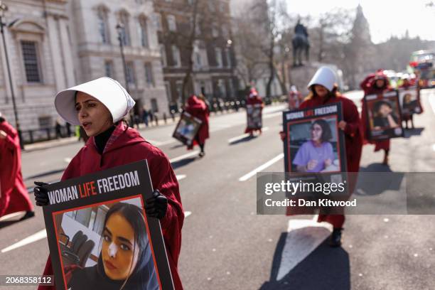 Protesters dressed as handmaids from The Handmaid's Tale hold signs reading "Woman Life Freedom" during a march from Parliament Square to Iran's...