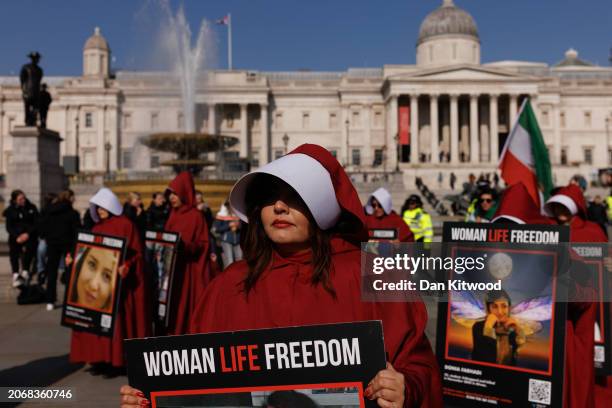 Protesters dressed as handmaids from The Handmaid's Tale hold signs reading "Woman Life Freedom" during a march from Parliament Square to Iran's...