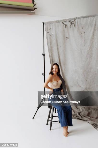 young female model posing in the studio in casual clothes: beige top and blue jeans. - hohlkehle stock-fotos und bilder