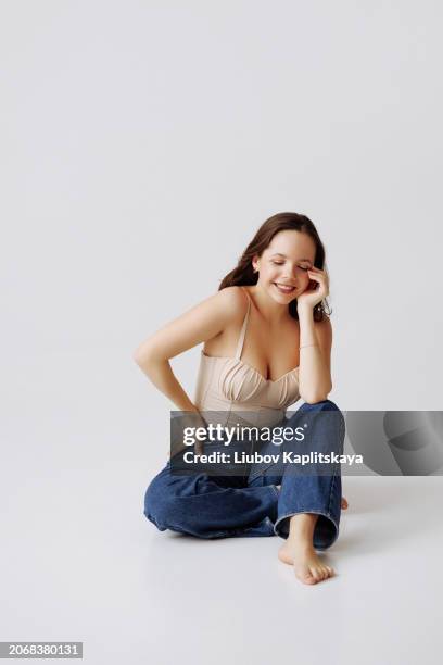 young female model posing in the studio in casual clothes: beige top and blue jeans. - cyclorama achtergrond stockfoto's en -beelden