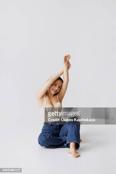 young female model posing in the studio in casual clothes: beige top and blue jeans. - cyclorama achtergrond stockfoto's en -beelden