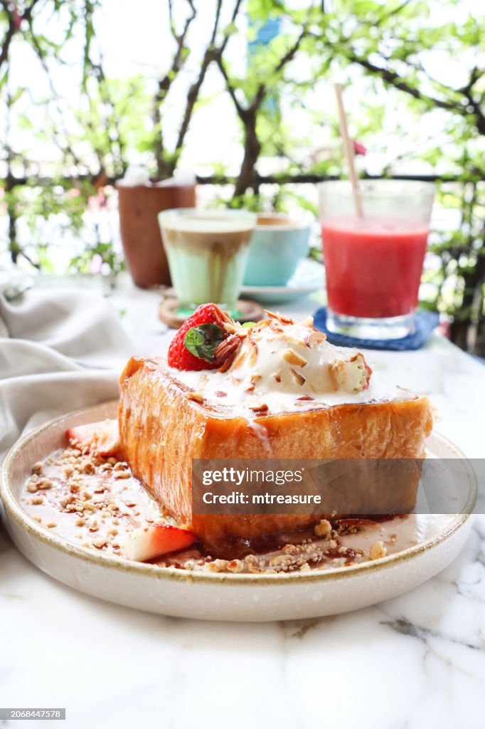 Close-up image white plate golden thick cut French toast, vanilla ice cream, strawberries and toasted almonds slices, American pancakes with whipped cream and fresh fruit, glasses of mint latte and strawberry and watermelon smoothie