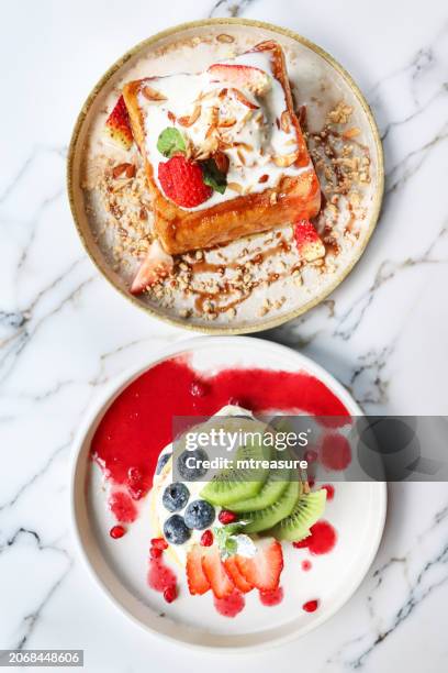 bild von weißen tellern mit goldenem, dick geschnittenem french toast mit vanilleeis, erdbeeren und gerösteten mandelscheiben, amerikanischen pfannkuchen mit schlagsahne und frischen früchten, auf weißer marmortischplatte, erhöhte ansicht - french toast stock-fotos und bilder