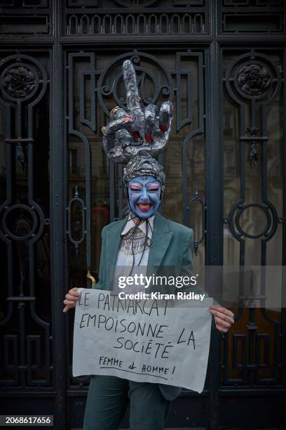 Protester poses for a photograph as they hold a placard which reads "Patriarchy Poisons Society" as thousands march through the streets of Paris to...