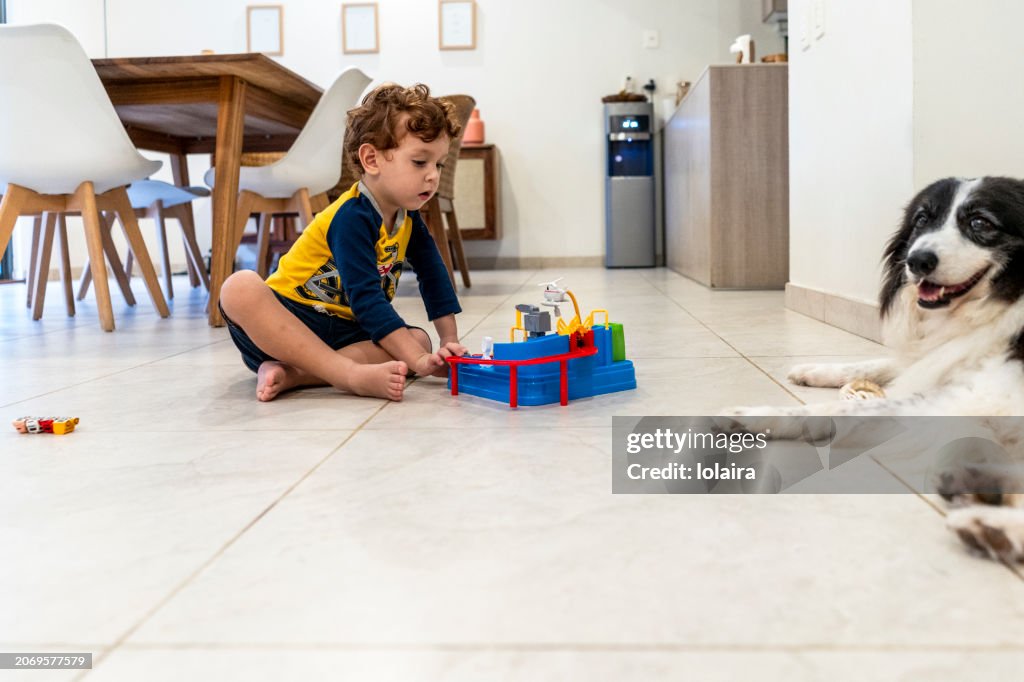 Redheaded child playing with toy and his dog lying on the floor