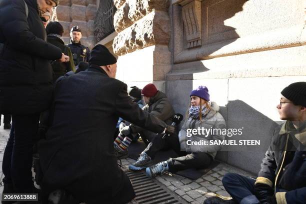 Swedish climate activist Greta Thunberg talks with a journalist as she sits outside the Swedish parliament, the Riksdagen, to demonstrate for climate...