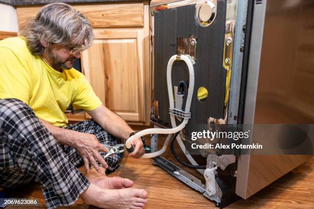 mature handyman cutting drain hose, repair a dishwasher on the kitchen floor - hose stock pictures, royalty-free photos & images