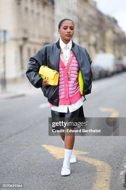 Guest wears a black bomber jacket , a white shirt, a yellow quilted leather Chanel bag, a pink tweed cardigan, a black leather skirt , white socks,...