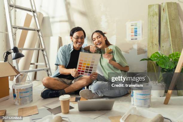 amante asiático matrimonio pareja sentarse relajarse elegir nuevo color después de la prueba pintar nuevo color nuevo apartamento casa reubicación mudarse en casa nueva, asia esposo esposa sentarse usando computadora portátil buscando ideas para la dec - renovación del hogar fotografías e imágenes de stock