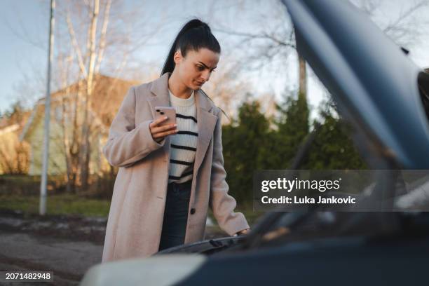 beautiful woman looking under the hood of the car since it broke down - vehicle breakdown stock pictures, royalty-free photos & images