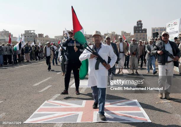 Yemen's Houthi followers from state servants carry weapons and step on a British Union Jack flag as they parade during a rally held against the...