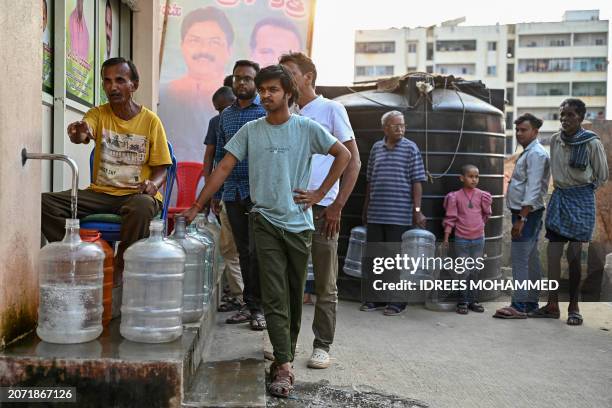 People stand in a queue with water cans to collect drinking water on subsidised rate amid an ongoing water crisis, at a water dispensing centre in...