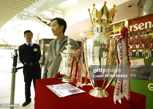 Soccer fan poses for a photo with the English Premier League trophy and the FA Cup, both held by Arsenal and on display in Hong Kong for two days, 18...