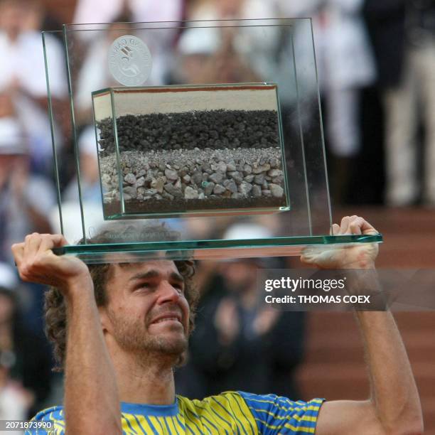 Brazilian player Gustavo Kuerten cries as he holds up a honorary trophy at the end of his French tennis Open first round match against French...