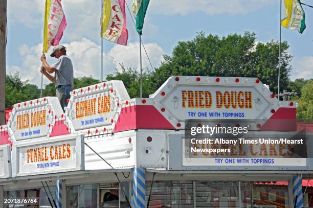 Patrick Wright of Brant, N.Y. Sets up the flags on top of the Fried Dough and Funnel Cakes business he works at the Altamont Fair on Sunday, Aug. 10,...