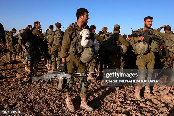An Israeli soldier carries a stuffed animal as he gathers along other soldiers after coming out from the Gaza Strip, near the border in southern...