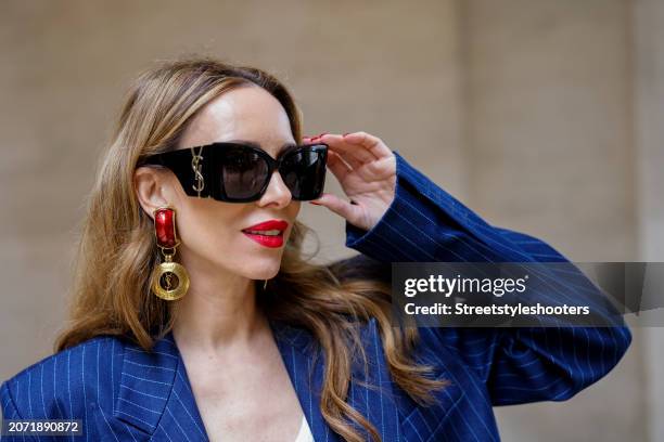 Alexandra Lapp is seen wearing a pinstripe blazer in navy by The Frankie Shop, a Colorful Standard tank top in white, Saint Laurent ear clips in red...