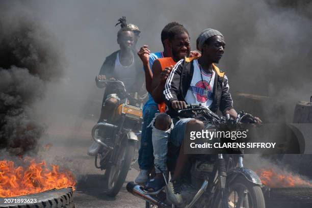 Men on motorcycles drive past by burning tires during a demonstration following the resignation of its Prime Minister Ariel Henry, in Port-au-Prince,...